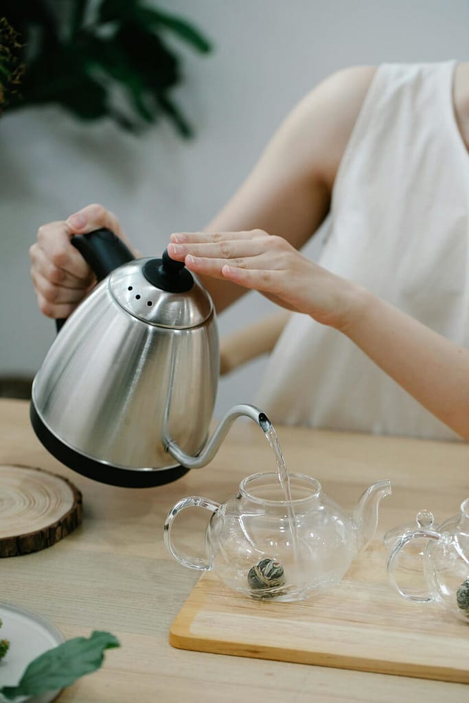 An electric kettle, a tea accessory for boiling water, is being used to pour water into a teapot